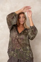 Blusa de gasa con estampado abstracto en tonos verdes y marrones, con detalles de hilos dorados. Presenta cuello camisero con escote en V, mangas largas con puños elásticos y un corte holgado.