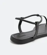 Sandalia plana de mujer color dorado metalizado, con diseño minimalista de tira fina que une la puntera y el empeine, y tira elástica fina alrededor del tobillo.