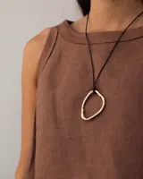 Collar con dije colgante de forma orgánica e irregular, acabado dorado, suspendido de un cordón negro de algodón natural.