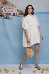 Vestido corto de lino color blanco, con cuello mao, cierre frontal de botones y tablillas decorativas en el pecho. Presenta mangas abullonadas a la altura del codo con terminación elástica y silueta evasé.