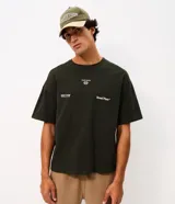 Remera de corte oversized color verde oscuro, con cuello redondo y mangas cortas. Presenta un diseño estampado en la espalda con tipografía en blanco y un pequeño logo gráfico en la parte inferior.