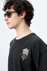 Remera negra de corte holgado con mangas cortas amplias y cuello redondo. Estampado pequeño de flor en el pecho y estampado grande en la espalda con diseño floral y texto.