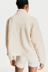 Campera deportiva color crema en tejido sherpa, de corte boxy, con cuello elevado, cierre frontal, bolsillo superior con cierre, bolsillos laterales insertados con cierre, elástico fino en los puños y cordón de ajuste en el bajo.