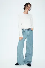 Jeans de tiro alto con diseño wide leg y cinco bolsillos. Presenta cierre frontal con cremallera y botón, e incluye un cinturón a contraste con hebilla metálica.