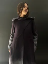 Tapado largo de lana merino color gris oscuro con teñido degradado en gris claro en ruedo, mangas y capucha. Tiene corte recto, bolsillos laterales y cierre cruzado con broches a presión ocultos en los hombros.