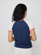 Remera azul marino de algodón con mangas cortas raglán blancas con ribete naranja y estampado ovalado con el logo de Rusty en el pecho.