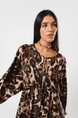 Vestido midi de corte holgado con estampado animal print en tonos marrones y beige. Tiene cuello redondo con lazo, mangas largas abullonadas y falda amplia con volantes. Incluye cinturón marrón con tachas.