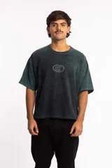 Remera de corte boxy fit, color negro con efecto lavado, de manga corta y cuello redondo. Presenta un logo bordado en el centro del pecho dentro de un óvalo.