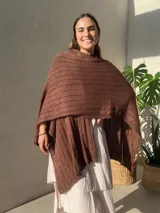 Ruana tejida en punto jersey, color negro con destellos brillantes de lurex. Presenta una etiqueta de cuero sintético con logo en la parte posterior.