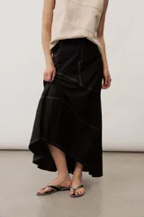 Falda larga negra de corte evasé, con costuras decorativas en contraste de color blanco y diseño asimétrico.