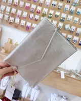 Sobre de fiesta tipo sobre con solapa triangular, acabado texturizado y color plateado metalizado. Incluye una correa de mano lateral.