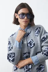 Cardigan de tejido jacquard color marrón con estampado floral en tonos rojo y rosado. Presenta cuello redondo, cierre frontal con botones y terminaciones acanaladas en puños y ruedo.