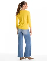 Buzo de tejido fino en color blanco, con cuello redondo y mangas tres cuartos tipo raglán. Presenta un detalle decorativo de tachas metálicas a lo largo de las mangas.