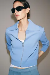 Chaqueta de punto color celeste con cuello solapa, manga larga y cierre frontal con cremallera. Acabados en rib.