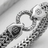 Pulsera de acero con diseño de cadena trenzada y cierre circular con detalles grabados.