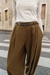 Pantalón de tiro medio con diseño bombacho, frunces delanteros y pierna abullonada con puños ajustados. Incluye bolsillos frontales y un cinturón decorativo con cadena metálica.