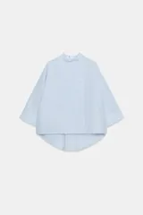 Camisa Zara Woman Collection de algodón con estampado de rayas verticales blancas y celestes. Presenta cuello perkins, mangas tres cuartos y un diseño asimétrico con cierre frontal cruzado mediante botones.