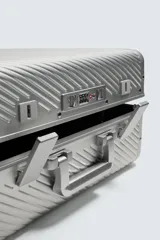 Maleta de cabina rígida fabricada en aluminio con diseño de líneas diagonales en relieve. Cuenta con cuatro ruedas giratorias, cierre TSA, compartimento principal con separador y asa telescópica.