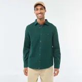 Camisa de manga larga de tejido gofrado en color verde oscuro, con cuello clásico, cierre frontal de botones y un bolsillo aplicado en el pecho.