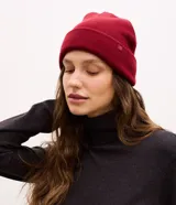 Gorro de punto tejido en color verde oliva, con diseño de borde plegado y una pequeña etiqueta rectangular aplicada en el frente.