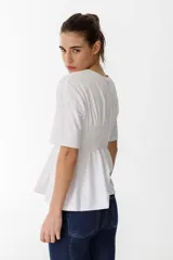 Remera blanca de algodón con cuello redondo, mangas cortas y detalle de fruncido tipo nido de abeja en la zona del busto, creando un efecto peplum.