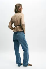 Chaqueta color beige con efecto ante, cuello redondo, manga larga y cierre frontal con cremallera. Presenta un bajo en evasé y un cinturón fino de cuero marrón oscuro con hebilla metálica.