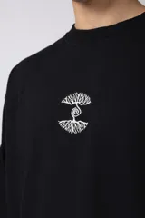 Remera de corte oversize confeccionada en algodón premium de gramaje pesado, color crudo. Presenta un bordado frontal pequeño en el centro del pecho con un diseño de dos árboles unidos por sus raíces y un parche estampado en la espalda con una silueta de mano fusionada con ramas.