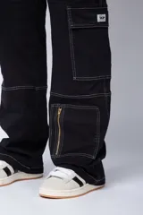 Pantalón tipo carpintero de corte relaxed fit y tiro medio, confeccionado en denim negro con costuras a contracolor en blanco. Presenta múltiples bolsillos cargo laterales, un bolsillo con cierre en la parte inferior y presillas utilitarias.