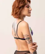 Corpiño de estilo deportivo con estampado tipo galaxia en tonos violeta, rosa y verde neón. Presenta un diseño con abertura frontal, bordes con detalle de puntilla negra y elástico negro en la base. Cuenta con breteles regulables y aros metálicos en la unión de los breteles.