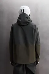 Cazadora deportiva de esquí con diseño bicolor en tonos negro y verde oliva. Presenta capucha amplia con visera, cierre frontal con cremallera termosellada, bolsillos frontales y en manga con cierres impermeables, y aberturas de ventilación en las axilas. Incluye faldón interior antinieve, puños ajustables y tecnología de rescate RECCO.