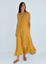 Vestido largo sin mangas de lino, con escote en V y diseño bicolor que combina un tono beige en el frente y un panel lateral en color fucsia. Presenta una costura central visible con detalle desflecado y un ruedo con volado.