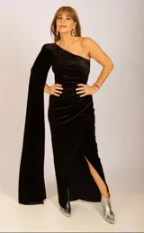 Vestido largo de fiesta negro de terciopelo, con corte asimétrico, un hombro descubierto y manga larga acampanada. Presenta tajo lateral y corte ajustado al cuerpo.
