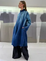 Tapado largo de fieltro de lana merino con teñido artesanal tie-dye en degradé de azul. Tiene cuello alto, cierre lateral con broches ocultos, bolsillos laterales y corte amplio.