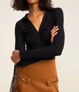 Body negro de rib, con cuello polo, escote en V, mangas largas y frunces en el busto. Cierre inferior con botones a presión.