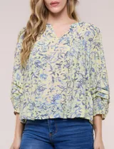 Blusa holgada de gasa estampada en tonos amarillos y azules, con cuello en V, mangas 3/4 abullonadas y alforzas horizontales.