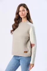 Buzo tejido de abrigo color beige, con cuello redondo, diseño de bloques de color en las mangas que combinan gris, blanco y beige, y detalle de etiqueta de cuero en el ruedo.