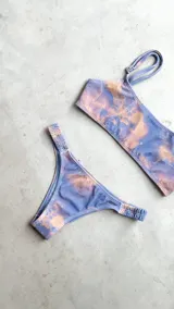 Conjunto de bikini con corpiño estilo bandó alto y breteles regulables, con lazo para atar en la espalda. La bombacha es vedetina con frunce elástico en los costados. Presenta un estampado tipo tie-dye o marmolado en tonos azules y naranjas/terracota.
