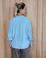 Blusa de manga larga con estampado de rayas verticales finas en tono beige. Presenta cuello redondo con volados, cierre frontal parcial con botones y puños con volados.
