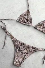 Conjunto de bikini con corpiño triangular de atar con apliques de argollitas y bombacha vedetina de atar con apliques de argollitas. El tejido presenta un estampado tie-dye o marmolado en tonos lila/azul y naranja/beige.