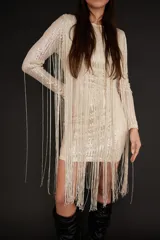 Vestido corto de manga larga confeccionado en tela con lentejuelas brillantes, caracterizado por sus largos flecos que caen desde los hombros hasta el ruedo. Presenta un corte ajustado al cuerpo y cuello redondo.