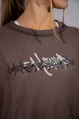 Buzo de tejido tipo waffle en color marrón, con corte holgado y estampa frontal con diseño de alambre de púas y tipografía gótica.