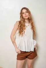 Blusa blanca sin mangas, con diseño transparente y detalles bordados florales en la parte superior, con vuelo y pliegues en la parte inferior.