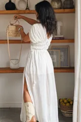 Vestido largo color blanco, con escote en V, mangas cortas abullonadas y cintura fruncida elastizada. Presenta detalles de encaje y cordones con borlas en el frente, además de una abertura lateral en la falda.