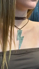 Gargantilla tipo choker con cordón de gamuza marrón y dije metálico grande en forma de rayo.