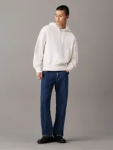 Buzo con capucha confeccionado en felpa de algodón regenerativo color blanco. Tiene corte relaxed, capucha con cordón, puños y bajo de canalé, logo bordado en el bajo en el mismo tono y estampado fotográfico digital de Calvin Klein en la parte trasera.