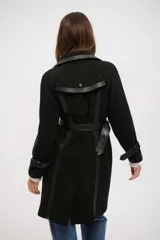 Tapado negro de corte cruzado con detalles en cuero sintético en solapas, puños y cierre frontal. Incluye cinturón ajustable con hebilla y botones metálicos.
