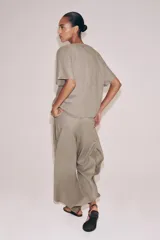 Top de lino de color beige, con cuello redondo, manga corta, bolsillos frontales aplicados y bajo ajustable con cordones. Cuenta con abertura en la espalda y cierre de botón.