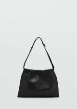 Bolso de hombro pequeño en piel ovino color negro, con diseño fruncido en la parte superior y asa ajustable con hebilla metálica.