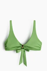 Top de bikini verde con tirantes ajustables, copas con relleno extraíble, frunces en los laterales, detalle metálico en el centro y tiras para anudar en la espalda.