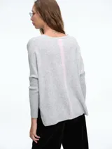 Sweater tejido de calce holgado con escote en V, mangas largas y tajos laterales en el ruedo. Presenta un diseño minimalista con detalle a contratono en la espalda.